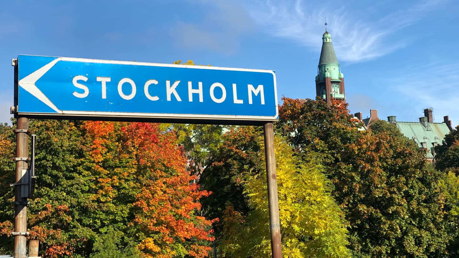 Road sign for Stockholm surrounded by trees with leaves changing colors