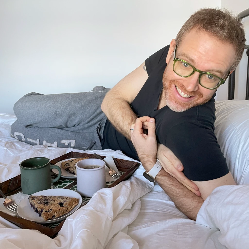 Arthur on bed smiling proudly beside breakfast tray with scones