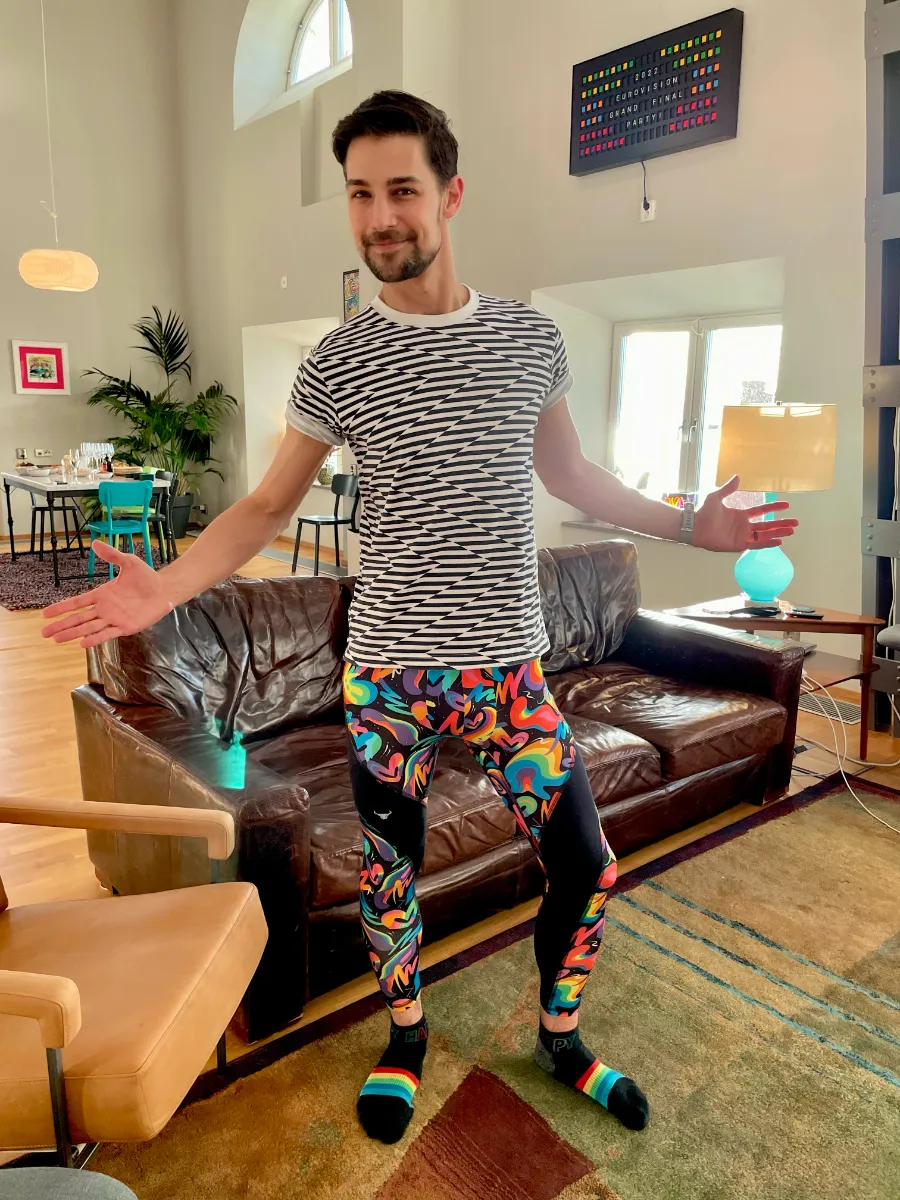 Jeremiah in a black and white striped shirt and rainbow colored tights standing in living room