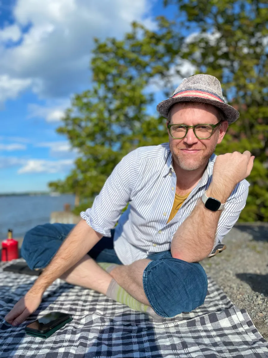 Arthur wearing hat sitting crossed-legged on picnic blanket