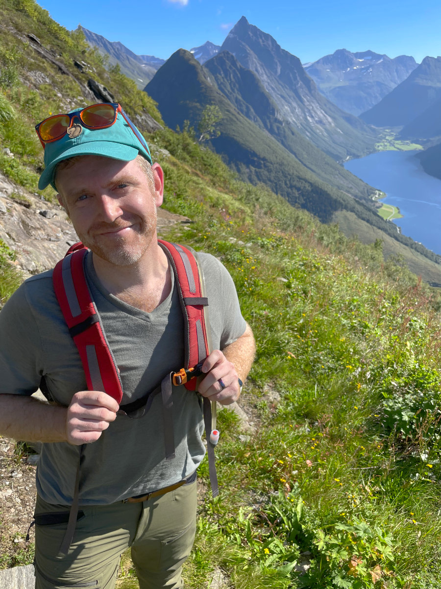 Arthur smiling on hiking trail. Mountains behind him.