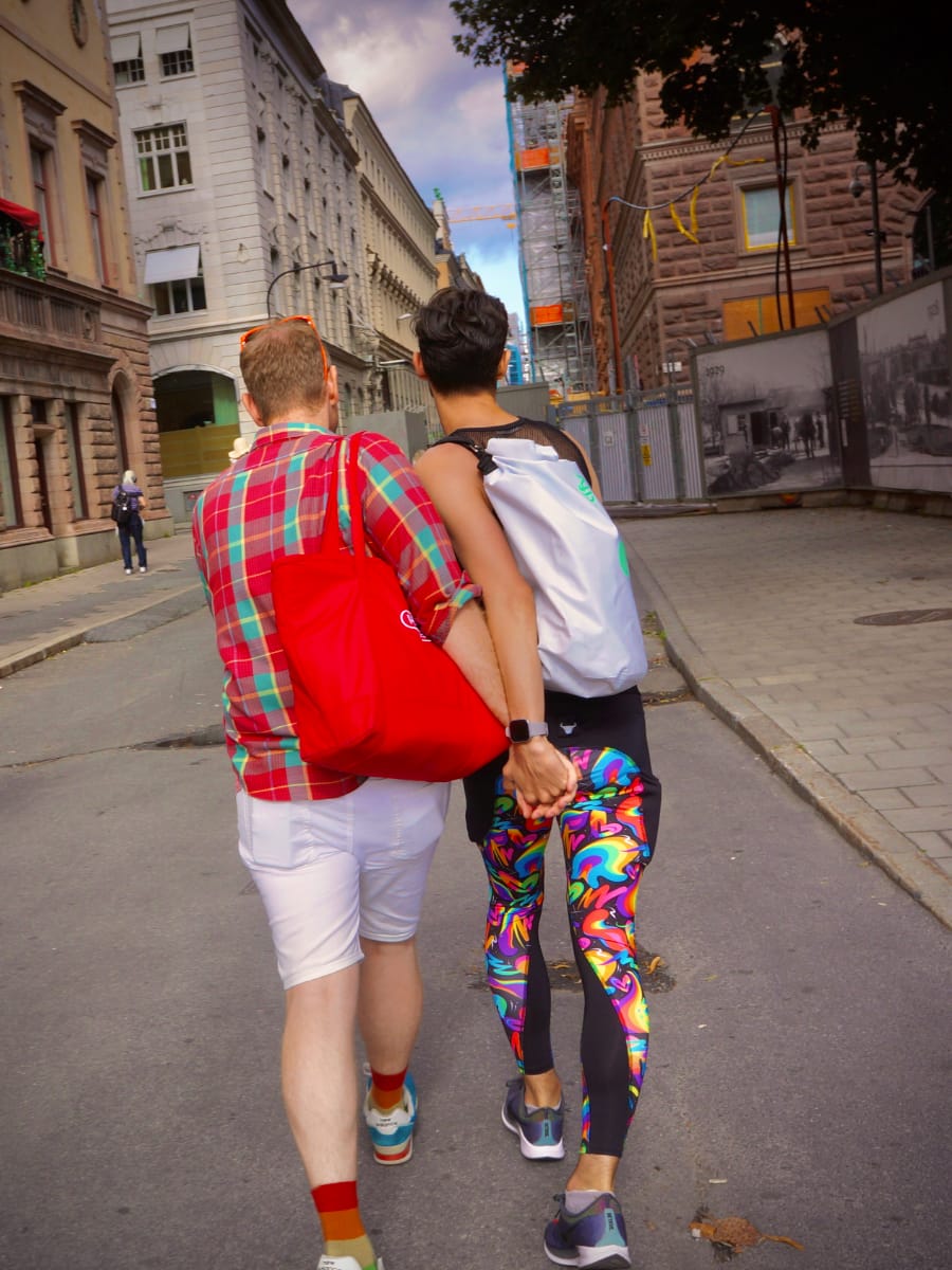 Arthur and Jeremiah holding hands as they walk away. They are wearing rainbow attire.