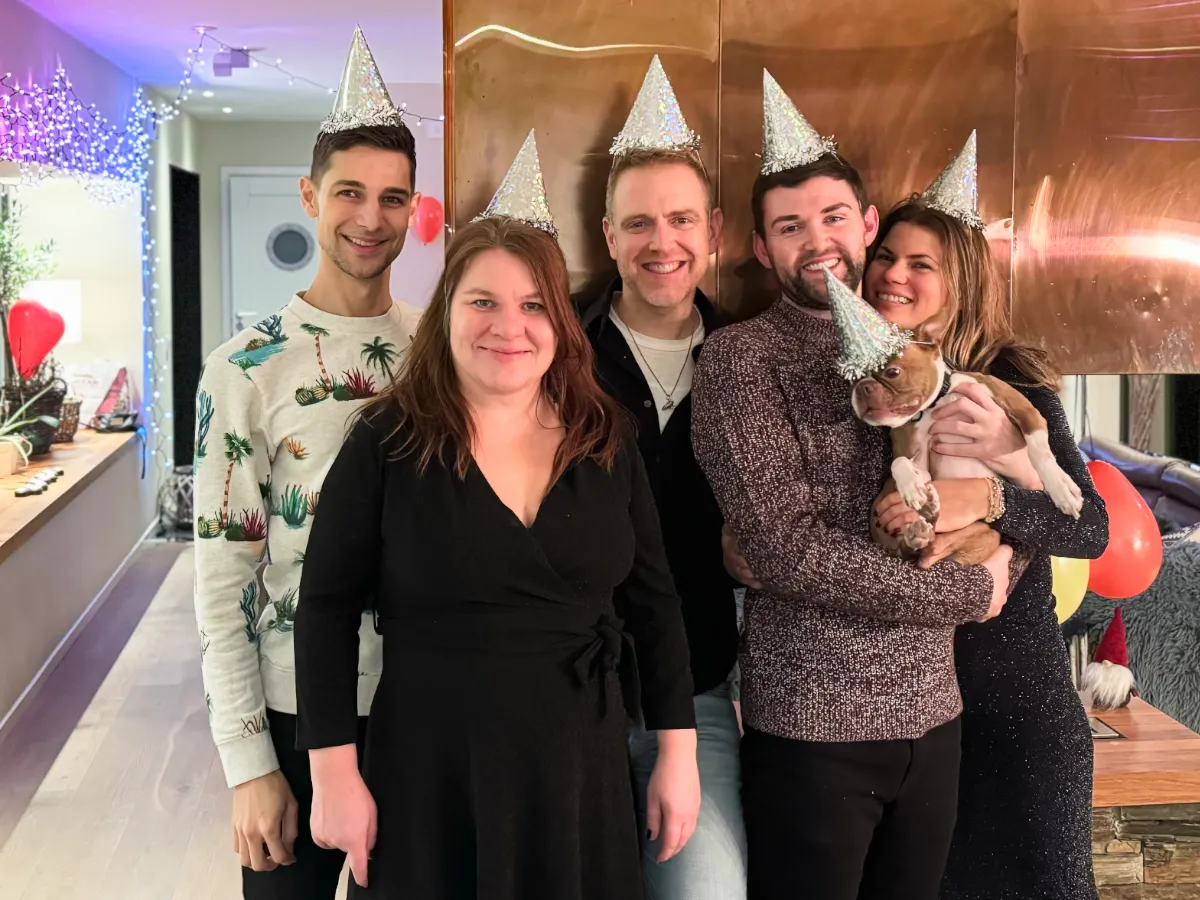 Jeremiah, Karin, Arthur, Wes, Finn, and Vendela wearing party hats with baloons and colored lights in the background