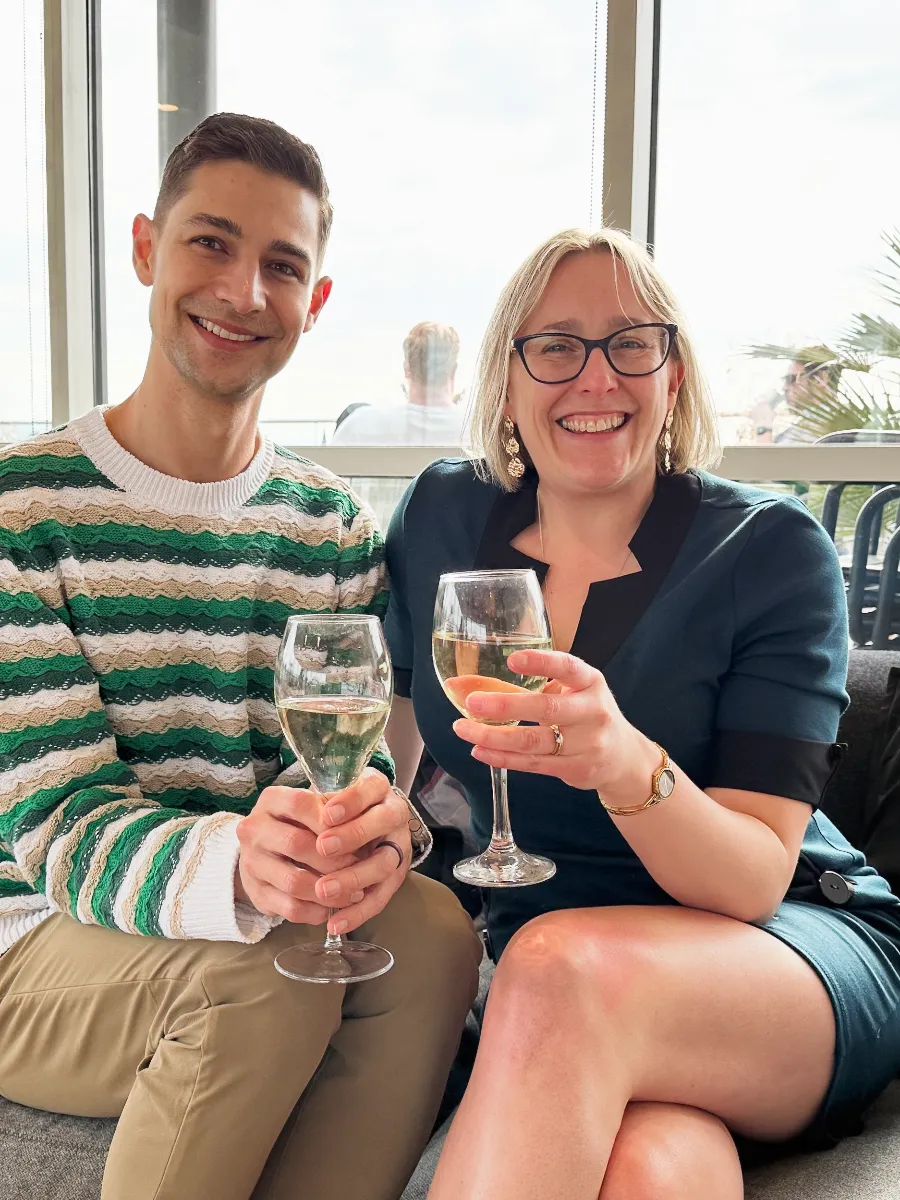 Jeremiah and Terry sitting on a sofa legs crossed holding glasses of wine