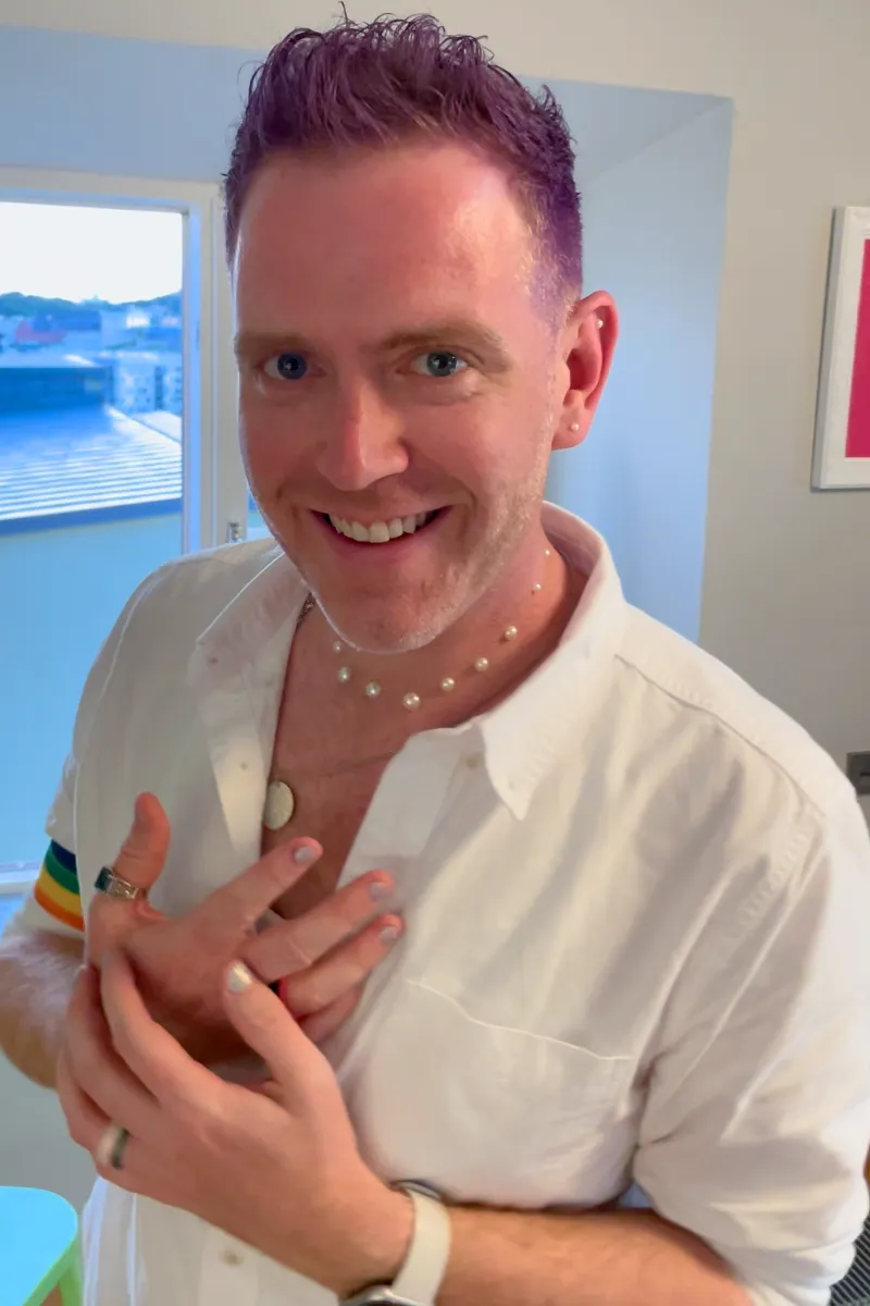 Arthur with purple hair, pearls glued onto his neck and ears, sparkly fingernails, and a rainbow arm band
