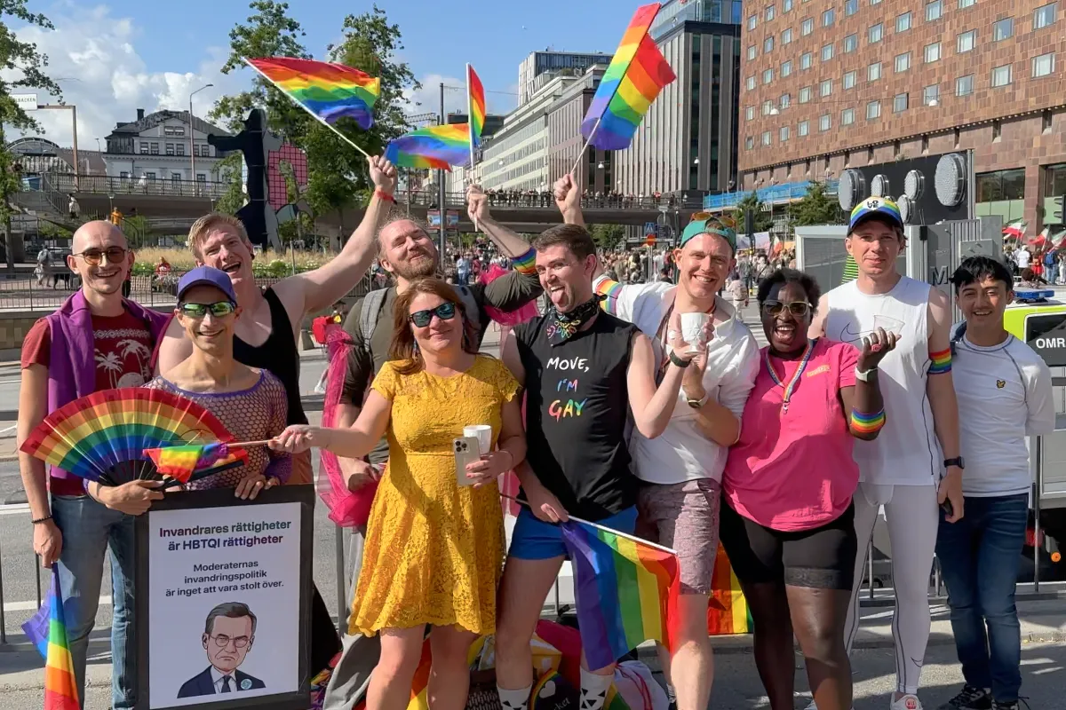 Group photo of people smiling in front of parade waving Pride flags