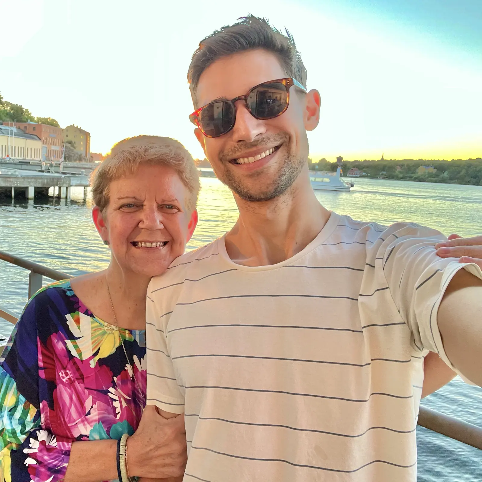 Gay and Jeremiah smiling together on Karin’s porch with the sun setting over the water behind them