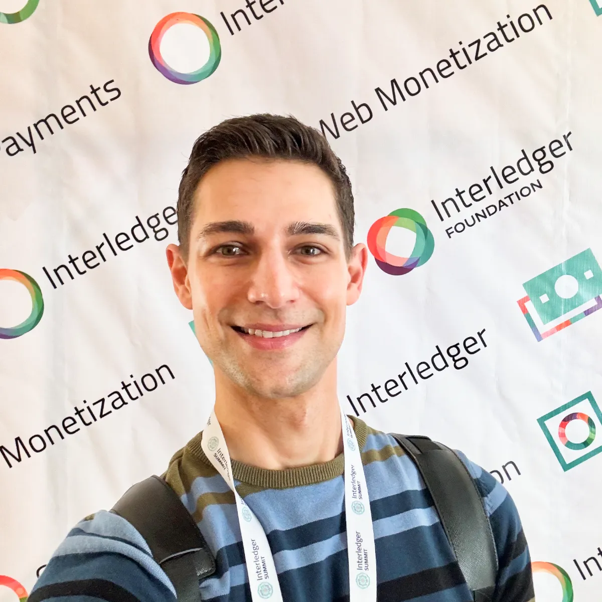 Jeremiah standing in front of step-and-repeat wall with logos of Interledger Foundation, Web Monetization, and Open Payments logos