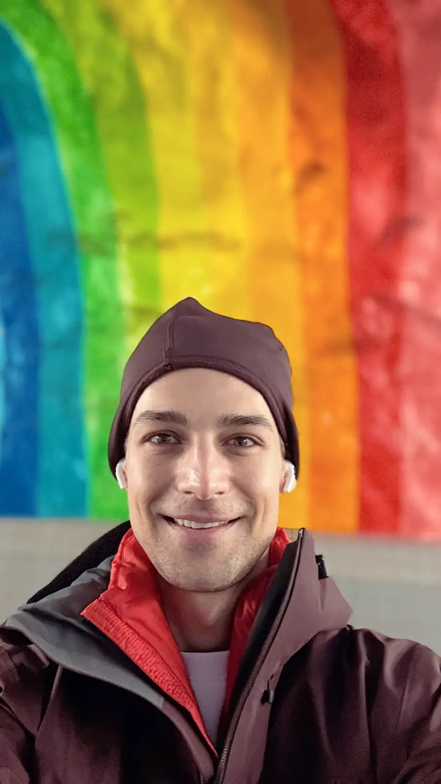 Jeremiah wearing winter hat and coat with rainbow mural behind him
